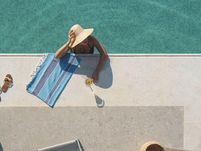 Persona con sombrero relajándose al borde de la piscina en una toalla junto a bebidas.