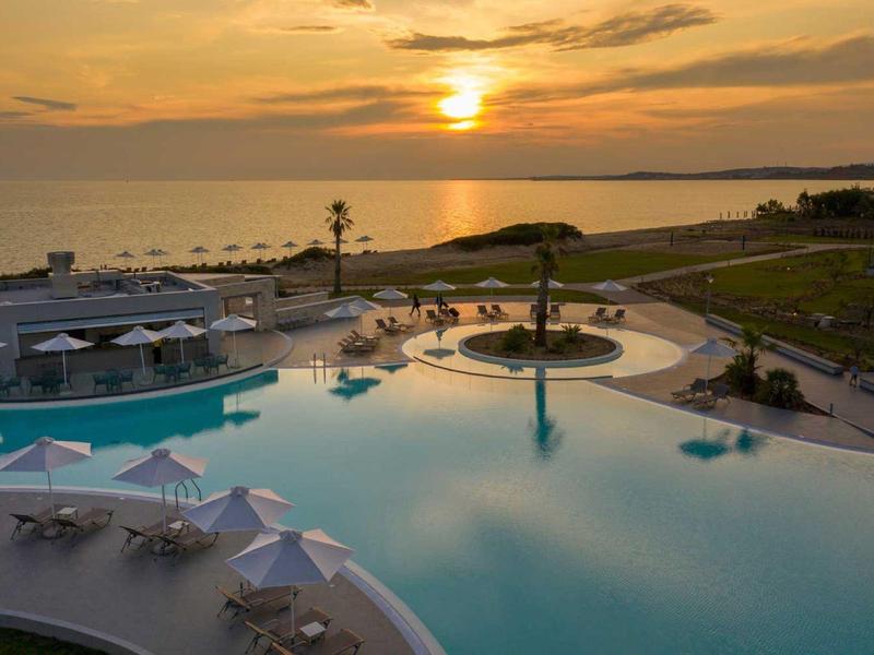 Gran piscina de hotel al atardecer con tumbonas y vistas al mar.