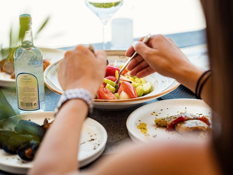 Persona comiendo ensalada con verduras frescas en mesa con botella de vino y alcachofa.