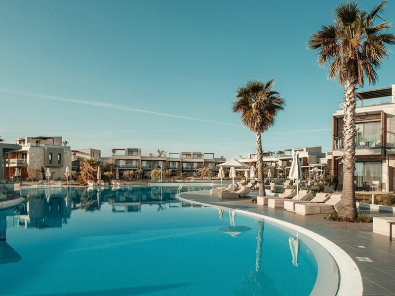 Piscina moderna de hotel con zonas de descanso y palmeras bajo un cielo despejado.