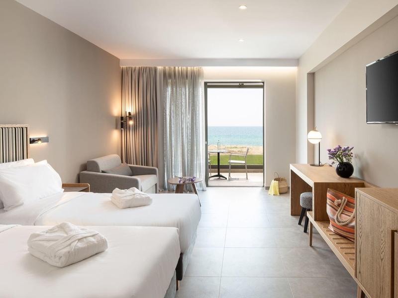 Habitación de hotel luminosa con dos camas, balcón y vista al mar.