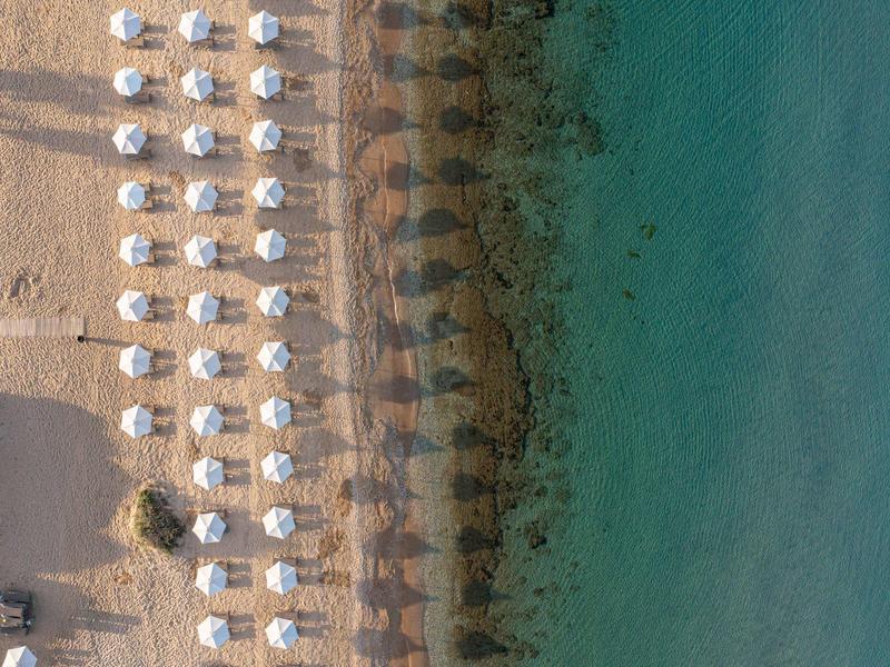 Vista aérea de una playa con filas de sombrillas blancas y agua turquesa.