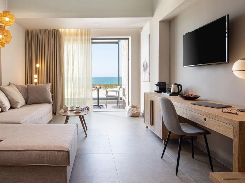 Habitación de hotel luminosa con sofá, escritorio y balcón con vista al mar.