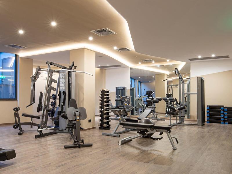Gimnasio moderno con pesas y máquinas de ejercicio en un área bien iluminada del hotel.