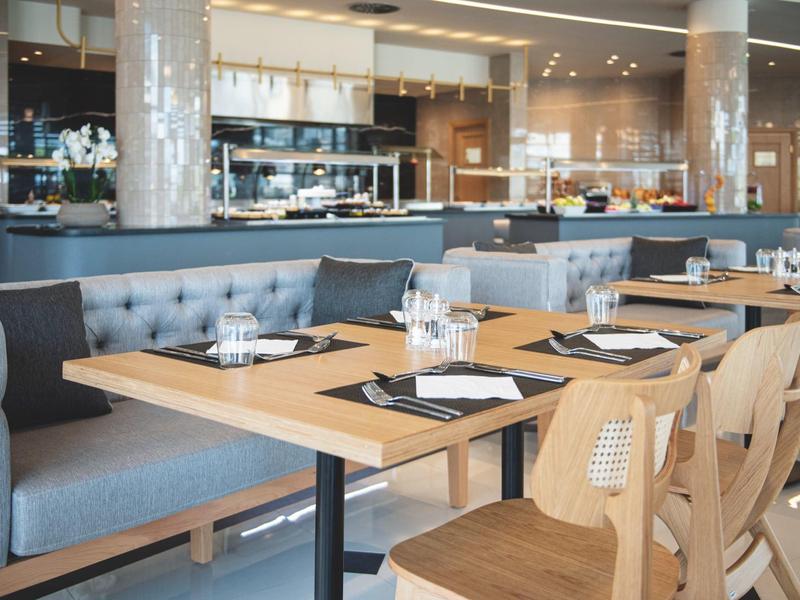 Restaurante moderno con mesas de madera y bancos en un interior luminoso de hotel.