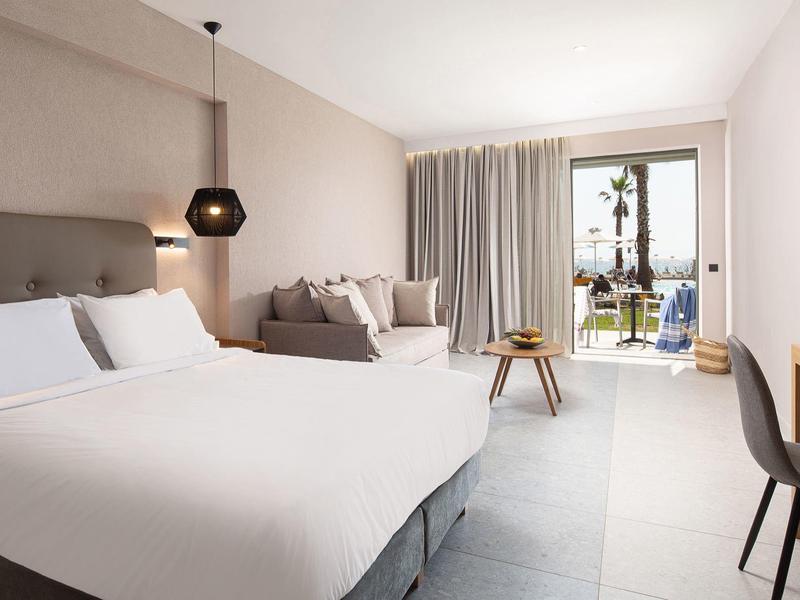 Habitación de hotel moderna con cama grande, zona de estar y vistas al balcón con vista al mar.