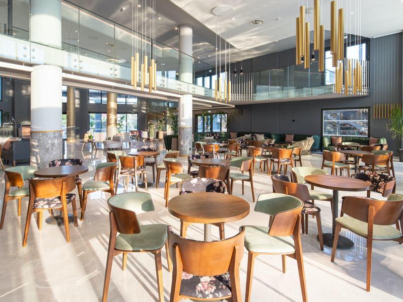 Área de restaurante de hotel moderna y luminosa con muebles de madera y grandes ventanales que permiten mucha luz natural.