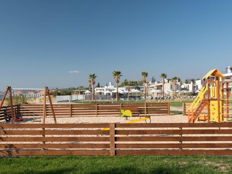Parque infantil con columpios, toboganes y arenero frente a un área residencial bajo un cielo despejado.