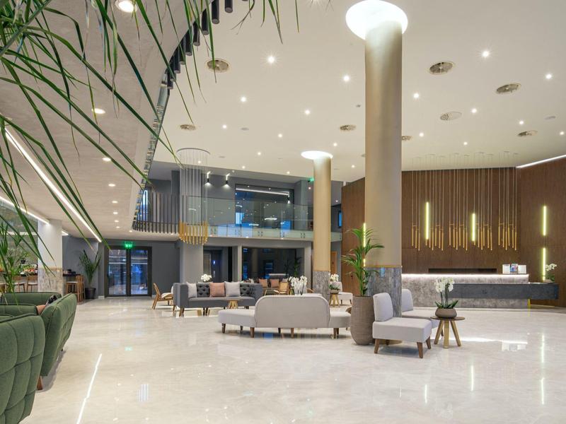 Amplia zona de vestíbulo de hotel con mobiliario moderno, asientos tapizados y suelos de mármol claro.