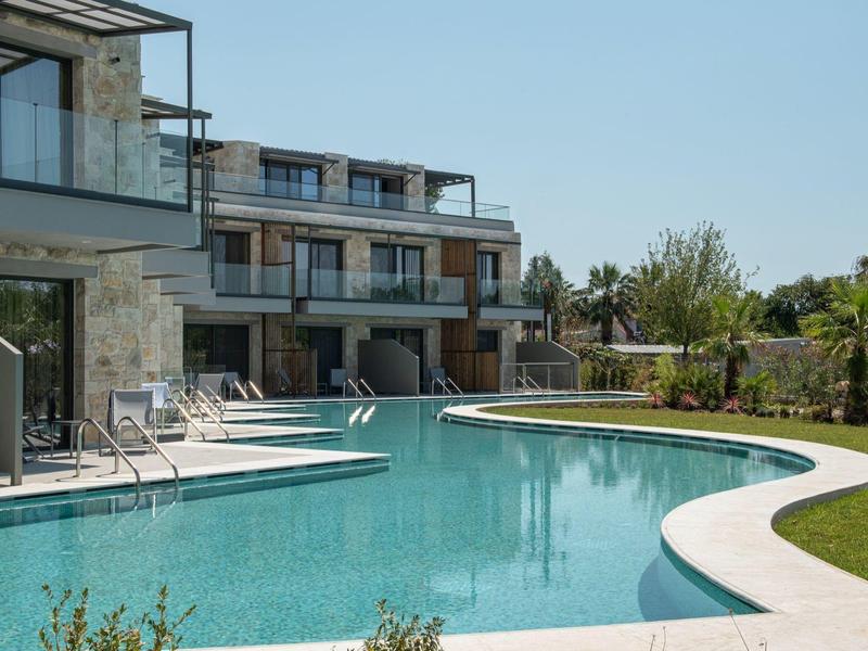 Piscina moderna de hotel con tumbonas, área verde alrededor y acceso directo a las habitaciones.