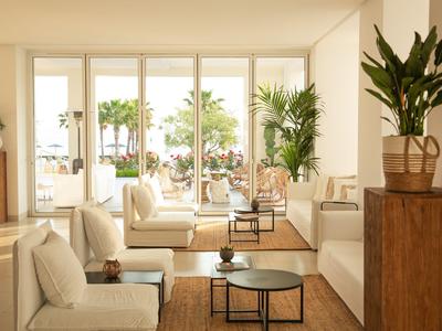 Heller Loungebereich mit bequemen weißen Sofas und Blick auf Terrasse mit Palmen.