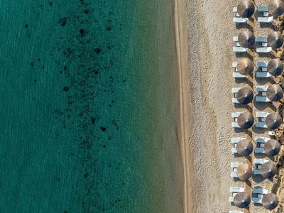 Aerial view of a beach with clear water and rows of umbrellas and lounge chairs.