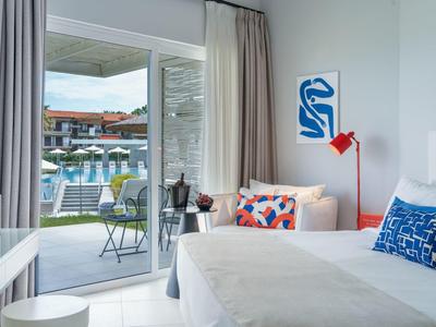 Bright hotel room with double bed, colorful decor, and terrace overlooking the pool.