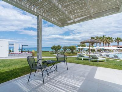 Terrace with two chairs, view of pool, lawn, and sea under blue sky.
