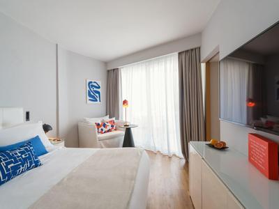 Modern hotel room with large bed, sofa, and window with curtains.