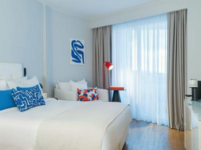 Bright, modern bedroom with large bed, colorful pillows, and daylight from large window.