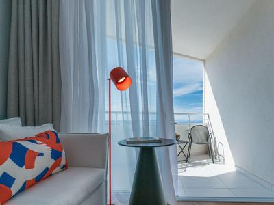 Bright hotel corner with modern chair next to glass side table and red floor lamp.