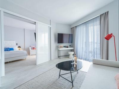 Modern hotel suite with living area, large glass wall, and adjoining bedroom.