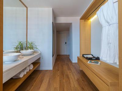 Modern hotel corridor with wooden floor, mirror, sinks, and bathrobes.