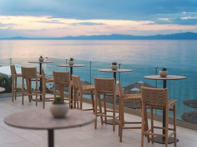 Blick auf eine Terrasse mit Tischen und Stühlen am Wasser bei Sonnenuntergang.