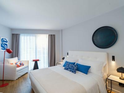 Bright hotel room with large bed, sofa, red lamps, and blue wall decoration.