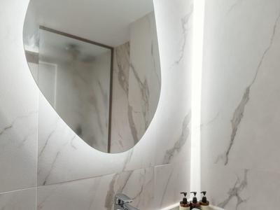 Modern bathroom corner with oval backlit mirror and black stone sink.