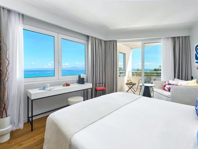 Bright hotel room with sea view, double bed, and seating area with balcony.
