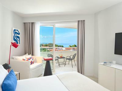 Bright hotel room with balcony, sea view, cozy couch, and modern TV.