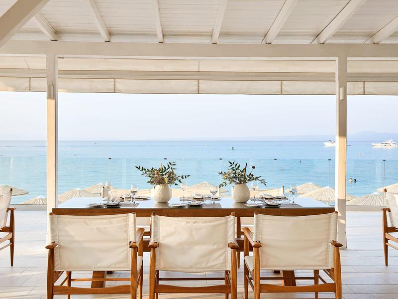 Beachside dining area with wooden chairs and a sea view under a shaded patio.