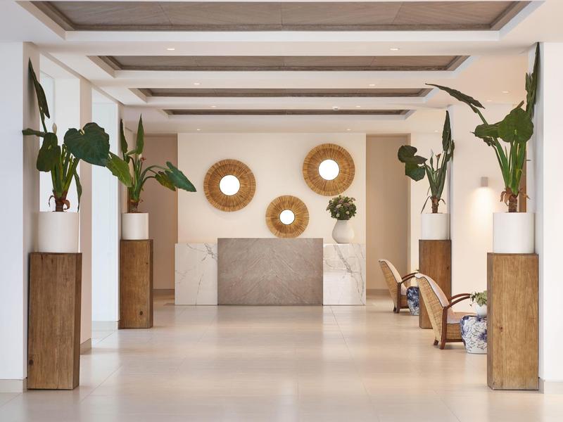 Minimalist hotel lobby with plants, wooden beams, circular wall decor, and seating area.