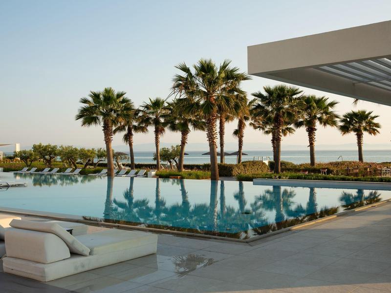 Modern infinity pool with palm trees and sun loungers overlooking the calm sea at sunset.