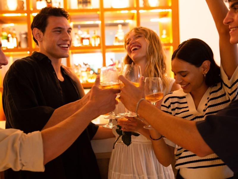 Group of friends enjoying drinks and laughing together in a warmly lit bar or lounge.