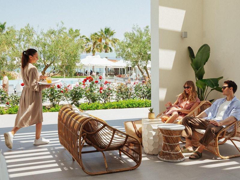 Guests relaxing in a modern outdoor lounge with rattan furniture and greenery in the background.