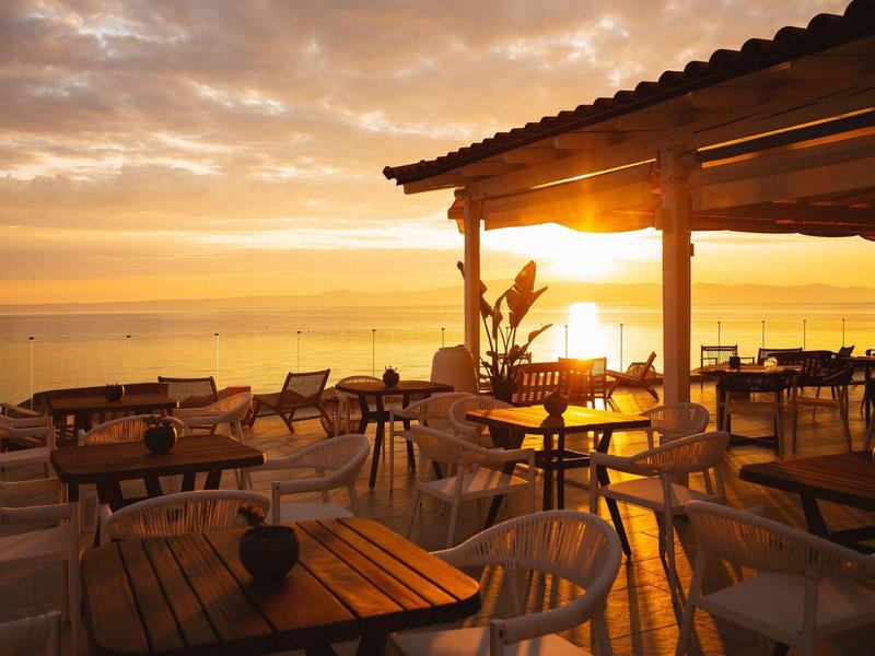 Terrace with tables and chairs at sunset overlooking the sea.