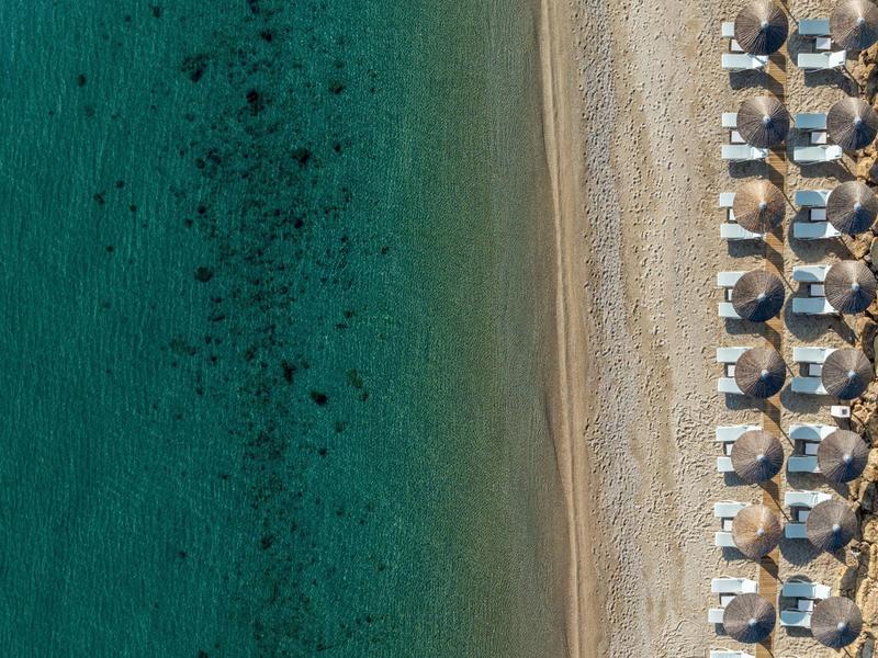 Aerial view of a beach with clear water and rows of umbrellas and lounge chairs.