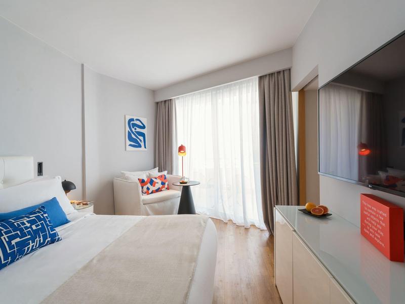 Modern hotel room with large bed, sofa, and window with curtains.