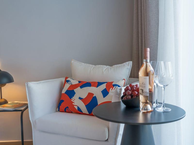 Cozy armchair with colorful pillow beside round table with wine and glasses.