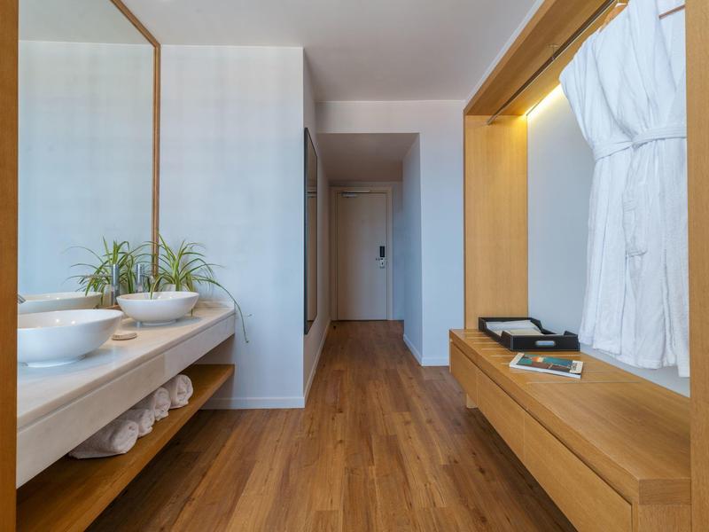 Modern hotel corridor with wooden floor, mirror, sinks, and bathrobes.