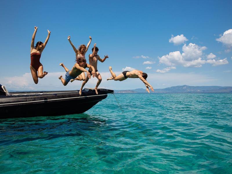 People jumping off a boat into clear blue sea under a sunny sky.