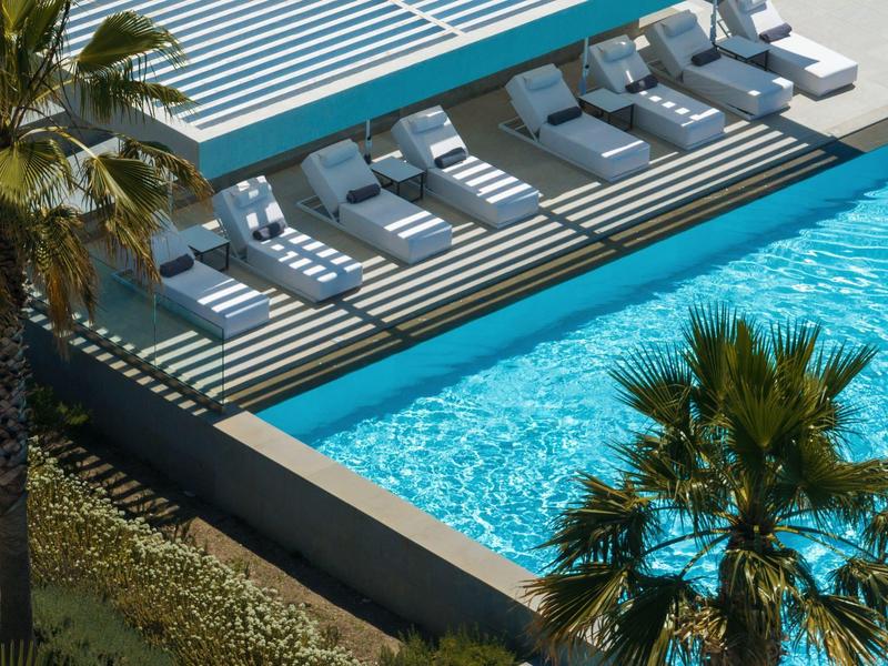 Modern pool area with loungers and palm trees at a hotel resort.