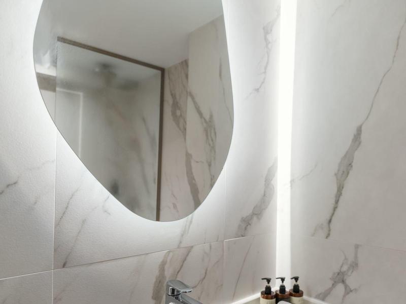 Modern bathroom corner with oval backlit mirror and black stone sink.