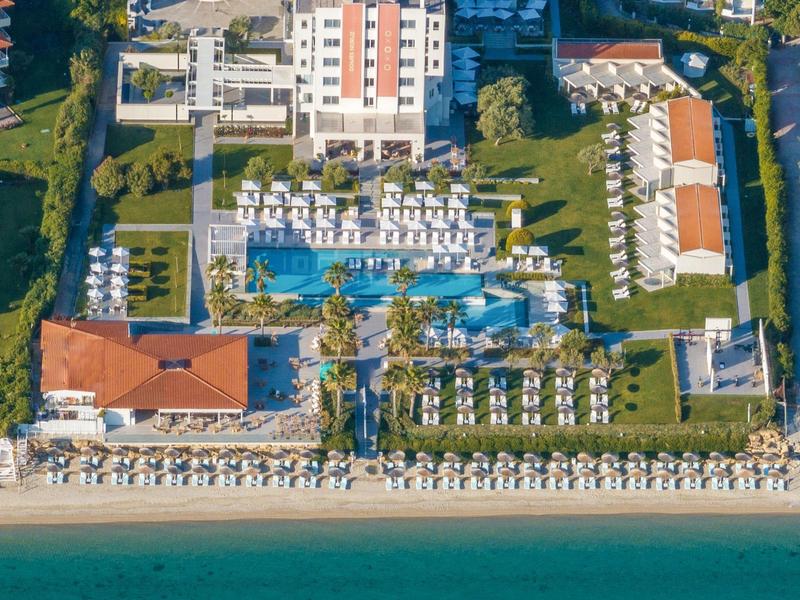 Aerial view of a hotel with large pools and sun loungers by the beach.
