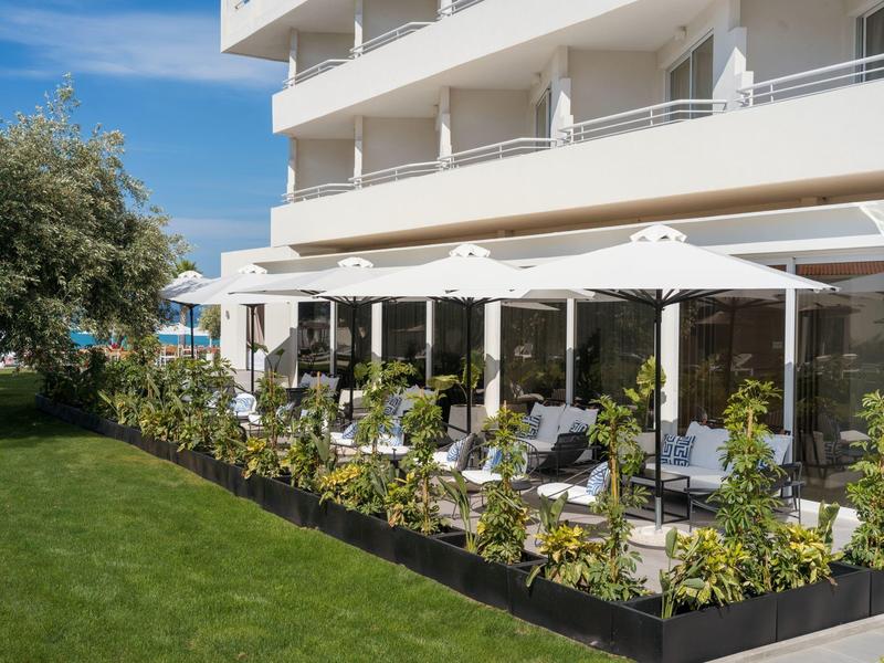 Green garden area with seating and umbrellas next to a multi-story hotel building.