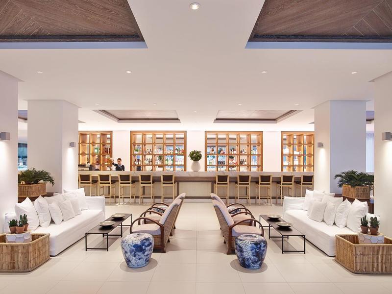 Spacious hotel lounge with white sofas, wooden tables, and elegant blue ceramic stools.