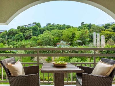Balcony with two chairs and table, view of green hills and trees.