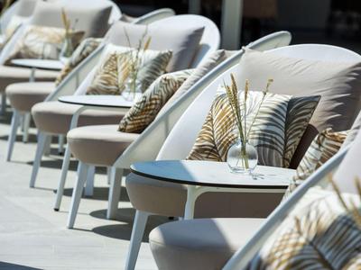 Row of comfortable lounge chairs with decorative pillows and small tables in an outdoor setting.