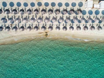 Row of sun loungers with blue umbrellas on sandy beach by turquoise water