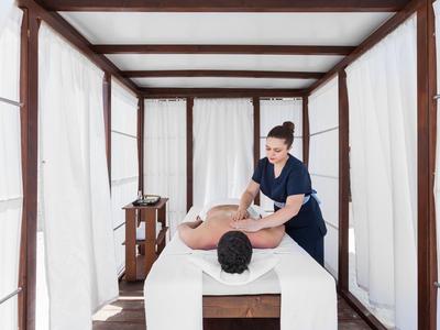 Masseuse treating a relaxed man in a bright, modern spa pavilion.