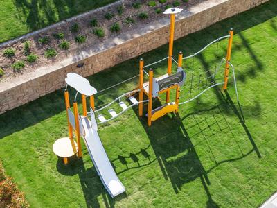 Modern playground with slide and climbing elements on green grass next to wall.