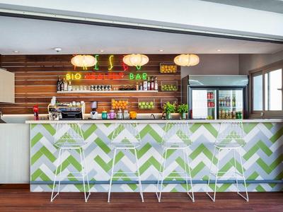 Modern hotel bar with green patterns, white bar stools, and illuminated shelves in the background.